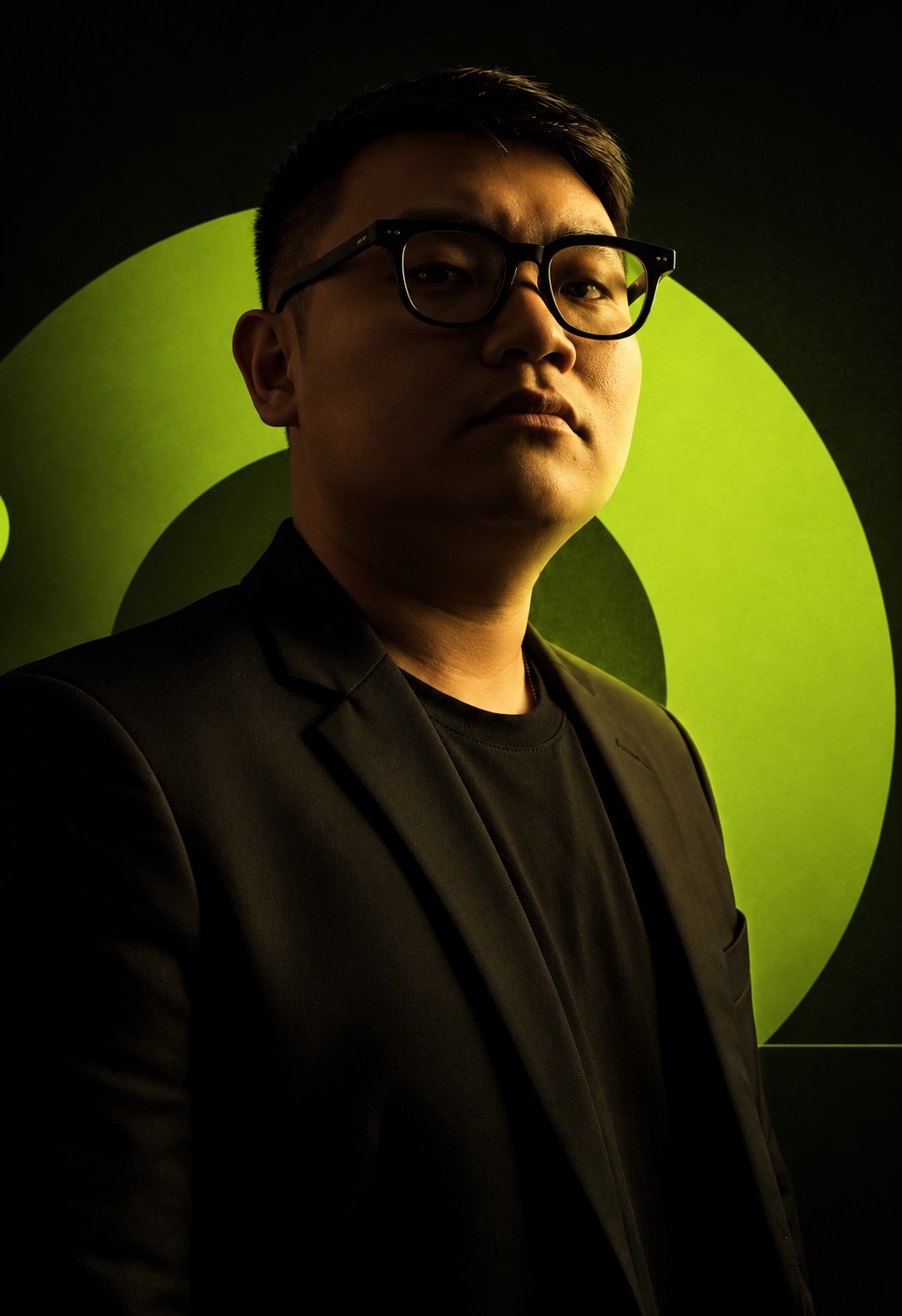 Khoa Phạm đeo kính, mặc blazer đen trên nền xanh lime